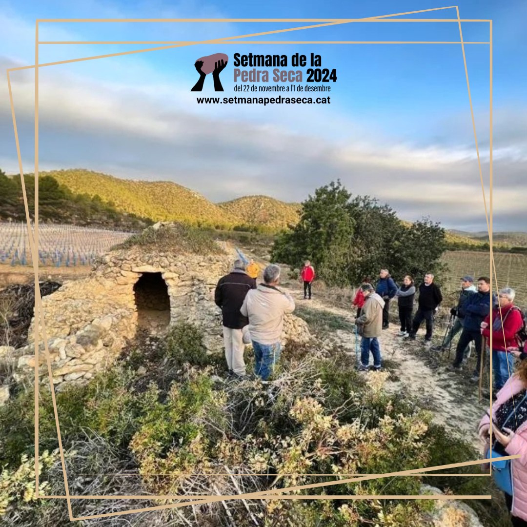 Grup de 9 persones que estan d'empeus, en un paisatge del Segrià. Escolten la presentació que fan dues persones sobre una cabana de pedra seca